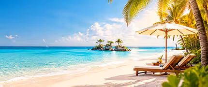 Sun loungers and a parasol on a white tropical beach beside calm turquoise sea, with a palm-topped islet offshore