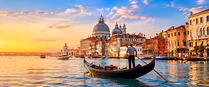 Gondolier steering a gondola along the Grand Canal at sunset with the Santa Maria della Salute basilica glowing in the golden light