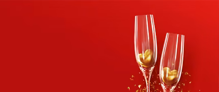 Two champagne flutes with gold heart decorations against a red background, Valentine’s Day holidays