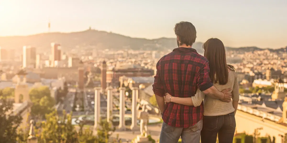 Couple embracing on Montjuïc hill overlooking Barcelona’s city skyline bathed in warm evening sunlight